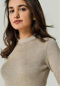 Beige geripptes Sweatshirt mit Rundhalsausschnitt, das eine enganliegende Silhouette und ein strukturiertes Gewebe aufweist. Sanfter, weicher Stoff mit langen Ärmeln.