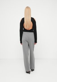 Top negro de manga larga con espalda descubierta, combinado con pantalones gris de pierna ancha. Tejido texturizado y ajuste relajado, zapatos negros elegantes de tacón alto.