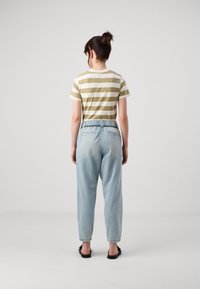 Randig olivgrön och vit t-shirt, ljusblå byxor med lös passform och elastisk midja, samt svarta platta sandaler. Bakvy mot en enkel bakgrund.