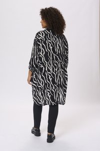 Chemise longue à rayures zèbre en noir et blanc avec des manches amples, portée avec des leggings noirs et des chaussures noires chunky. Tissu lisse et léger.