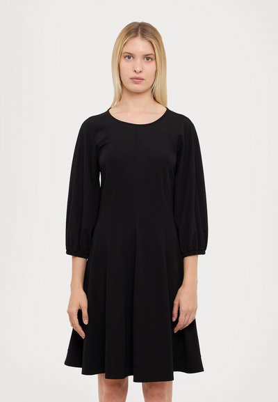 Robes noires en tissu doux avec un décolleté rond, des manches ballon et une jupe évasée arrivant au genou. Présente une texture lisse.