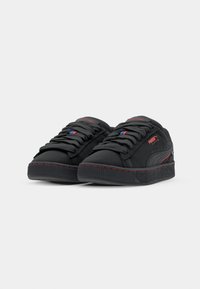 Pair of black Puma Suede sneakers with red accents, thick textured soles, and black laces on plain white background.