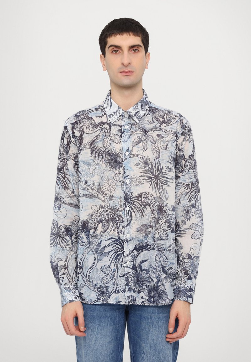 Camicia con bottoni in tessuto leggero, caratterizzata da una stampa botanica blu e nera, maniche lunghe e colletto curato. Indossata con jeans di jeans.
