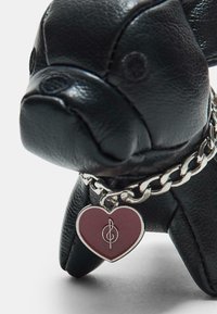 Figurina di cane in pelle nera con dettagli testurizzati, dotata di una catena in argento e di un ciondolo a forma di cuore in burgundy con un design a nota musicale.