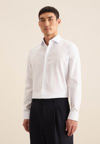 Biała koszula z długim rękawem w jasne pionowe paski, z zapięciem na guziki i dopasowanym kroju; w połączeniu z ciemnymi spodniami o gładkiej fakturze.