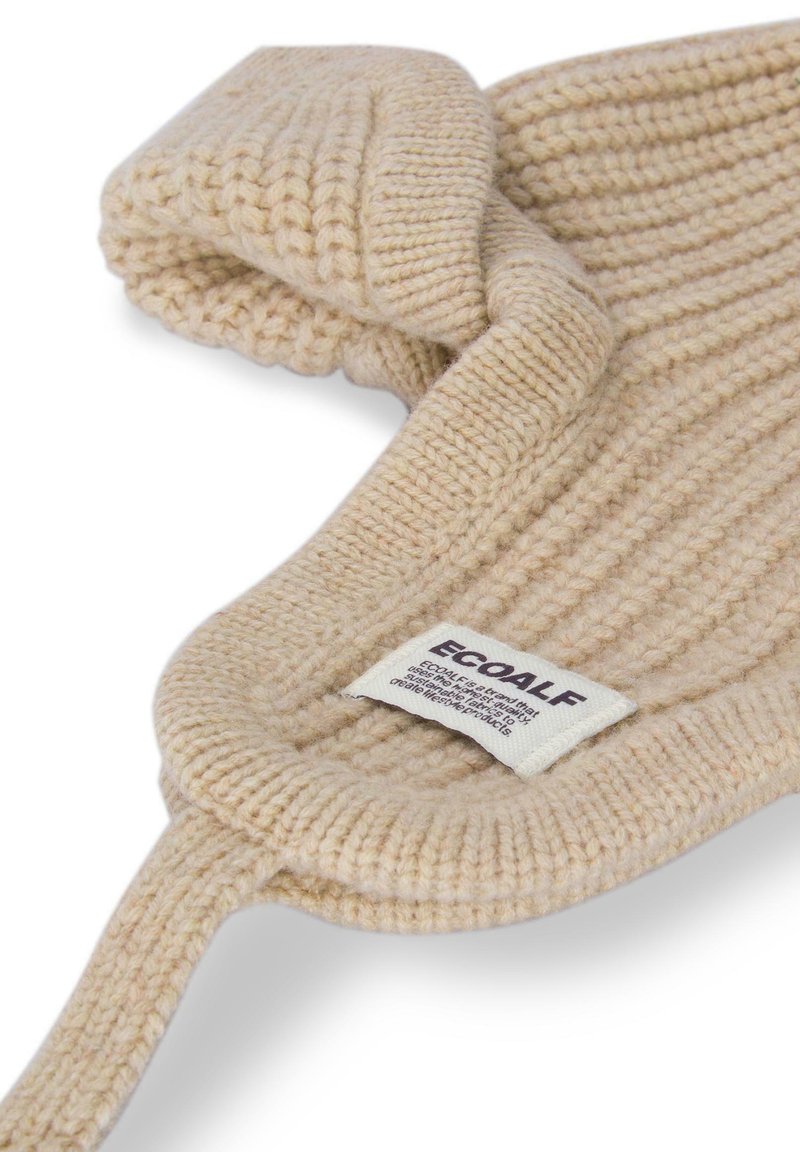 Beżowy, dziany szalik o ryflowanej fakturze, z pętelkowym wzorem i widoczną metką. Miękki materiał, idealny na chłodniejsze dni.