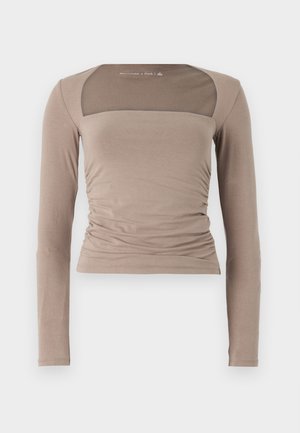 Long-sleeve top in light beige with a square neckline, ruched side details, and transparent mesh accents on the shoulders. Smooth texture.