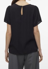 Blouse noire à manches courtes avec un dos en découpe en trou de serrure, en tissu doux et texturé avec une coupe ample. Dotée d'un ourlet arrondi et de plis subtils.