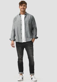 Gray button-up shirt over a white T-shirt, black denim jeans with rolled cuffs, and white sneakers with black accents.