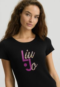 Juodas trumpomis rankovėmis marškinėliai su ryškiu "Liu Jo" logotipu, papuoštu leopardų raštu, ir apvaliu iškirpimu. Minkšta, lygi medžiaga.