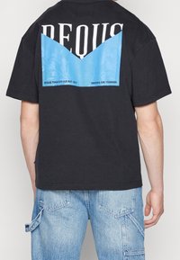 Camiseta de algodón negra con un gráfico azul en la parte posterior que incluye texto. El diseño presenta letras en blanco audaces y una textura suave.