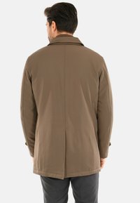 Giacca leggera marrone con taglio sartoriale, dotata di collo a revers e tessuto liscio. Dettaglio spacco posteriore visibile.