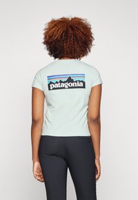 T-shirt bleu clair à manches courtes avec un logo Patagonia noir au dos, décoré de graphismes colorés de montagne et une coupe ajustée.