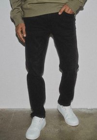 Jeans neri in denim, con un taglio slim e una texture sottile, abbinati a sneakers bianche. La parte superiore è nascosta alla vista.
