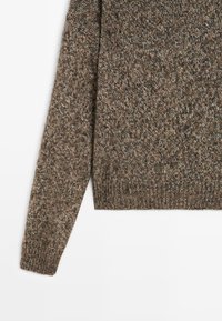 Pletený svetr v texturované hnědé směsi s různými odstíny. Má ribbaný lem a manžety. Dlouhé rukávy a klasický kulatý výstřih.