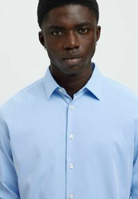 Jasnoniebieska koszula zapinana na guziki z delikatną fakturą w paski i standardowym kołnierzykiem. Posiada białe guziki oraz dopasowany krój.