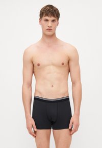 Black cotton boxer briefs with a fitted design, featuring a striped elastic waistband and a front pouch. Smooth texture.