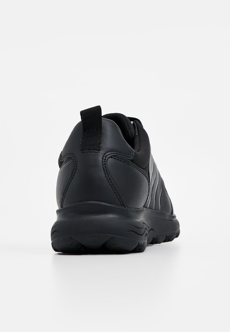 Chaussures de sport noires avec une tige en cuir lisse, un col rembourré, des panneaux latéraux texturés et une semelle en caoutchouc robuste. Anse au niveau du talon.