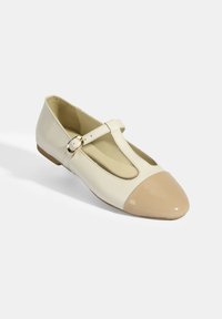 Cremfarbene Leder-Flatschuhe mit einer beigen Lackkappe, T-Riemen-Design und goldener Schnalle. Weiche Innenauskleidung für Komfort.