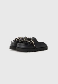 Pantofi negri slip-on cu o talpă din cauciuc texturat, împodobiți cu detalii din mărgele argintii și negre pe partea superioară. Design rotund și finisaj neted.