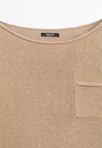 Beiger Strickpullover mit rundem Halsausschnitt, kleiner Brusttasche und schwarzem Etikett mit der Aufschrift "Massimo Dutti Made in China."