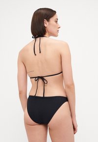 Svart to-delt bikinitruse med strukturert stoff, halterneck-bånd og justerbar rygg med kryssdesign. Klassisk badetøysform.