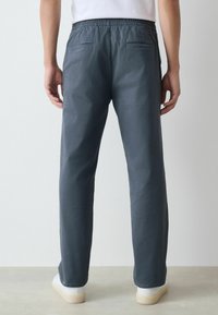 Sötétszürke nadrág elasztikus derékpánttal, egyenes lábakkal, két hátsó zsebbel, fehér sportcipővel viselve. Simaság jellemzi.