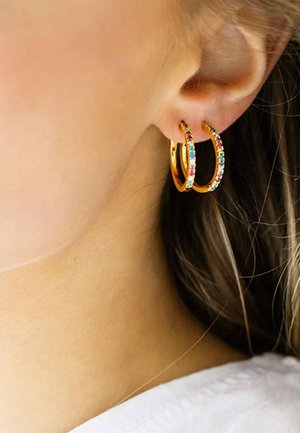 Guld hoops øreringe prydet med multicolor rhinestones, store og runde, vist på en models øre med en glat hudtone.