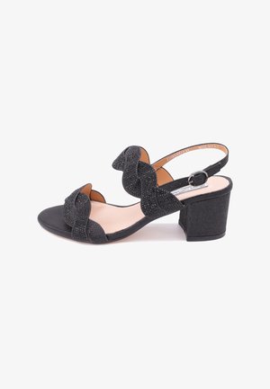 Sandal con tacco alto nero, realizzata in tessuto testurizzato, con design a fascia ondulata e fibbia alla caviglia. Presenta un tacco a blocco basso e una soletta liscia di colore marrone chiaro.
