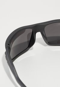 Schwarze Sonnenbrille mit matter Textur, eckigem Rahmen und dunklen Gläsern; verfügt über dezente Hardware-Akzente an den Seiten.