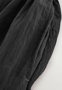 Gros plan d'une manche en tissu noir froissé avec couture visible sur fond blanc.