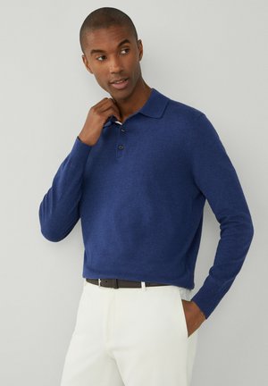 Blå langærmet polo t-shirt i blødt materiale, med krave og tre knapper. Komplementeret af lyse bukser.