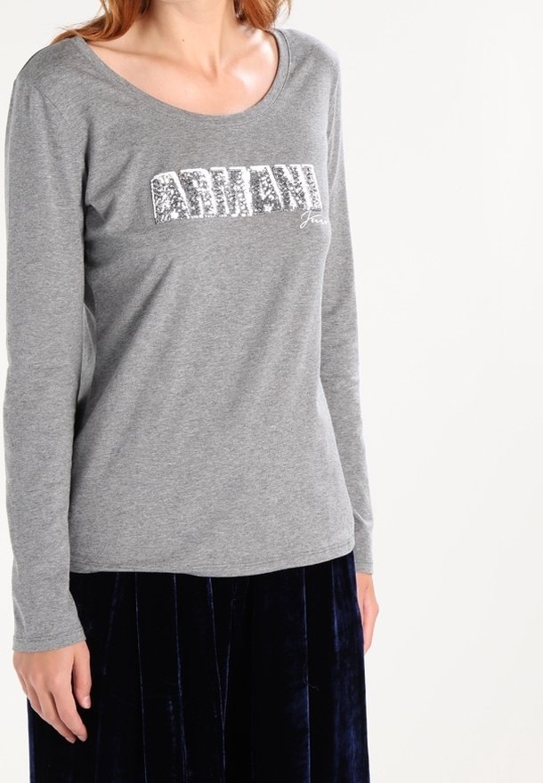 Szary długi rękaw T-shirt z szerokim dekoltem i błyszczącym logo "ARMANI Jeans" w kolorze srebrnym, zestawiony z ciemną aksamitną spódnicą.