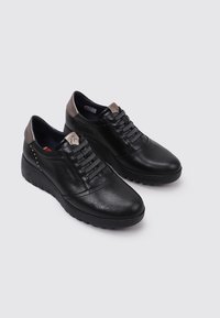Chaussures en cuir noir avec une finition texturée, dotées d'un laçage et d'un empiècement de talon gris contrastant orné de clous décoratifs.