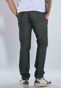 Dark grey pants with a straight cut, made of textured fabric, featuring two back pockets with button closures, paired with light sneakers.