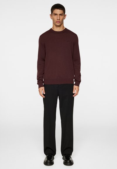 Bordeaux sweater met een ronde halslijn en lange mouwen, gedragen over zwarte broek. De stof lijkt zacht en textuur te hebben.