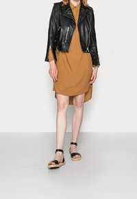 Veste de motard en cuir noir sur une robe chemise marron, associée à des sandales noires à lanières. Accent sur le contraste des textures et des couleurs.