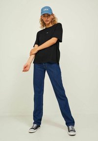 Black short-sleeve t-shirt with a small logo, paired with straight-leg blue jeans and black sneakers, complemented by a light blue baseball cap.