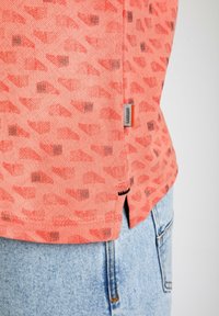 Koraalpatroon shirt met een geometrisch ontwerp en donkere accenten, gemaakt van zachte stof, met een zijlabel waarop "GABBAINO" staat.