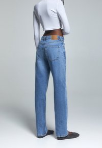 Jeans de mezclilla de tiro alto, de color azul claro, con un corte relajado, que cuentan con bolsillos traseros y un parche de cuero marrón en la cintura.