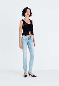 Fekete horgolt cropped top, megkötős részletekkel, világoskék, testhez simuló farmernadrággal és hegyes orrú fekete magassarkúval párosítva. Simogató, laza stílus.