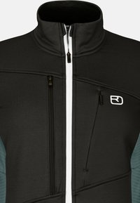 Schwarze und türkisfarbene Zip-Jacke mit hohem Kragen, strukturiertem Stoff und kontrastierendem weißen Reißverschluss. Verfügt über zwei Reißverschlusstaschen auf der Vorderseite.