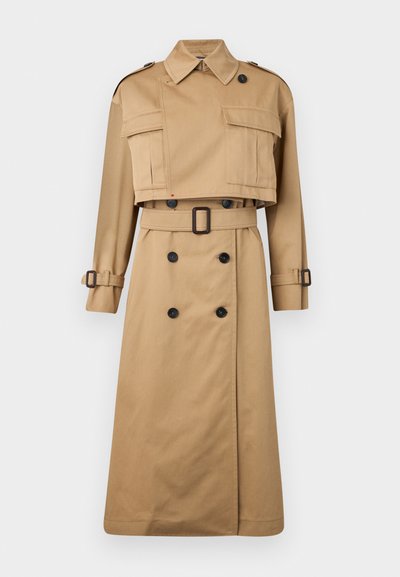 Beige trench coat with cropped jacket top, large front pockets, and long sleeves. Features a belted waist and double-breasted button closure.