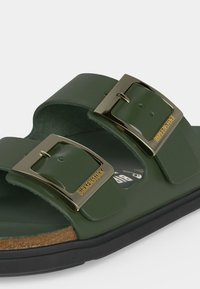 Тъмнозелен сандал Birkenstock с две регулируеми метални катарами и черна подметка на бял фон.