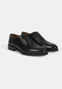 Chaussures habillées en cuir noir avec une finition lisse, un design à lacets, un bout arrondi et des accents de couture subtils. Talon plat et semelle texturée.