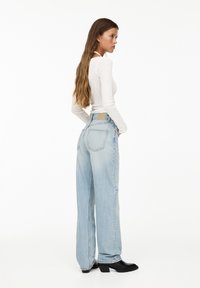 Ljusblått högmidjat jeans med vida ben, en bakficka och en beige lapp vid midjan. Bärs med en åtsittande vit långärmad topp.
