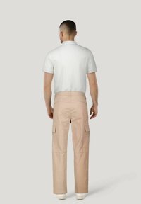 Lichtbeige cargobroek met zijzakken, gecombineerd met een kortemouwen witte polo. Gladde textuur en relaxte pasvorm.