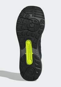 Sort gummisål til sneakers med et gult accent og tekstureret grebmønster, der har et centralt torsionselement for stabilitet.