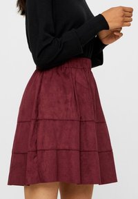 Bordeaux, gelaagde rok gemaakt van een zacht, suède-achtig materiaal. Voorzien van een elastische tailleband en horizontale naaddetails.