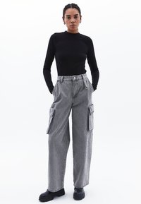 Top nero a maniche lunghe abbinato a pantaloni cargo larghi grigi chiari con tasche laterali e vita alta, completato da stivali neri.